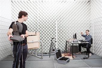 The picture shows two male students in a silent room [anechoic chamber] of the faculty of media.